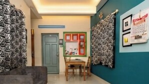 Um quarto com sofá, mesa e cadeiras, porta e um mural com papéis.