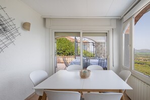 Ein Essbereich mit einem weißen Tisch und Stühlen, einem Korbwäscheschrank und Blick auf eine Terrasse mit Sitzgelegenheiten und einer Steinmauer.