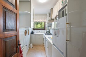 Eine schmale Küche mit weißen Schränken, einem Herd und einem Kühlschrank.