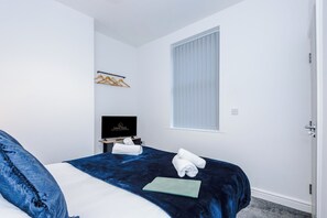 A hotel room with a bed, a television, a window with blinds, and a door. - Spacious Home with Free Parking | Atherton House (Greater Manchester)