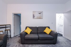 A living room with a grey sofa, two yellow cushions, a painting on the wall, and a door leading to another room. - Spacious Home with Free Parking | Atherton House (Greater Manchester)