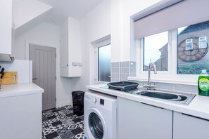 Een kleine keuken met een wasmachine, een spoelbak en een raam met uitzicht op een bakstenen gebouw.