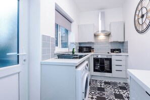 A compact kitchen with white cabinets, a microwave, a built-in oven, and a washing machine. - Spacious Home with Free Parking | Atherton House (Greater Manchester)