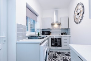 A compact kitchen with white cabinetry, a built-in oven, a microwave, and a black and white patterned floor. - Spacious Home with Free Parking | Atherton House (Greater Manchester)
