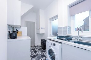Une cuisine moderne équipée d’un lave-linge, d’un évier et d’une fenêtre.