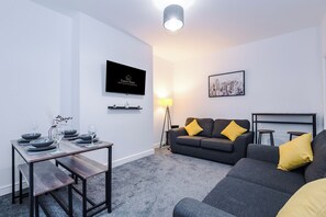 Un salon moderne comprenant un canapé, une table basse, un téléviseur fixé au mur et un coin repas avec une table dressée pour deux personnes.