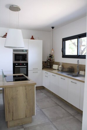 Eine moderne Küche mit weißen Schränken, einem eingebauten Ofen, einer Spüle und einem Fenster mit Blick auf Bäume.