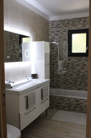 Une salle de bain moderne avec un grand miroir, un meuble-lavabo blanc, une baignoire et une douche.