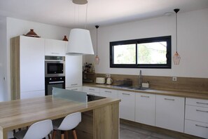 A modern kitchen with white cabinetry, a wooden countertop, a built-in oven, and a window above the sink. - A Haven of Peace in the South C1S (Vernègues)