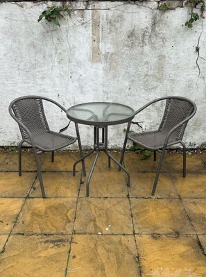 A round table with two chairs in a patio area with a concrete floor and a white wall with some greenery. - Spacious Stay by the Docks | Your Wallasey Getaway (Liverpool / Merseyside)