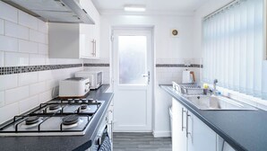 A compact kitchen with white cabinets, a gas stove, a microwave, and a sink. - Rishton Stay | Shops & Transport | Near Blackburn (Lancashire)