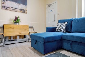 Une pièce avec un canapé bleu, un bureau en bois orné d’une plante et une porte blanche.