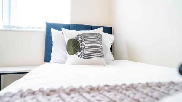 A neatly made bed with a blue headboard and white bedding, including a pillow with a circular design. - Rishton Stay | Shops & Transport | Near Blackburn (Lancashire)