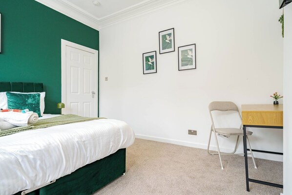 Un dormitorio con una cama, un escritorio y una silla. Hay tres cuadros en la pared.