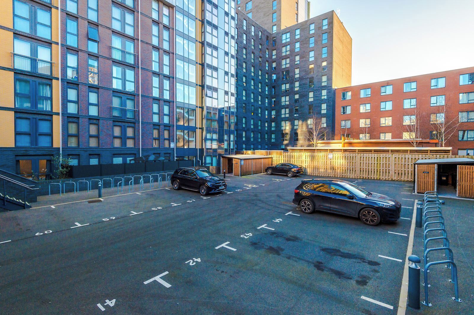 A parking area with multiple cars, a building with a modern design, and a wooden fence.