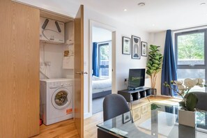 Ett modernt hotellrum med tvättmaskin, en platt-TV, en matplats och ett stort fönster med utsikt.
