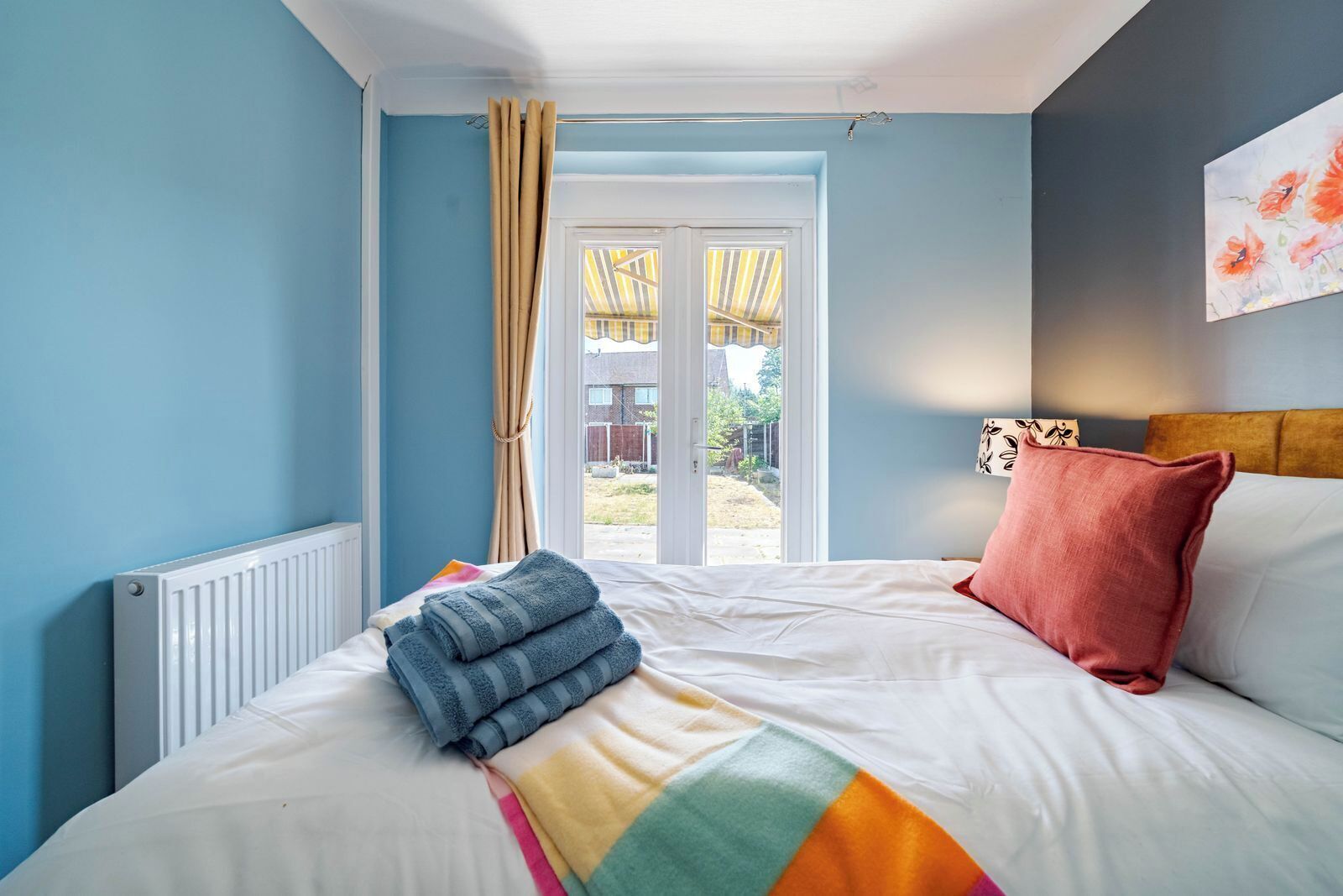 A bedroom with a bed, a window with curtains, a radiator, and a view of the outside.