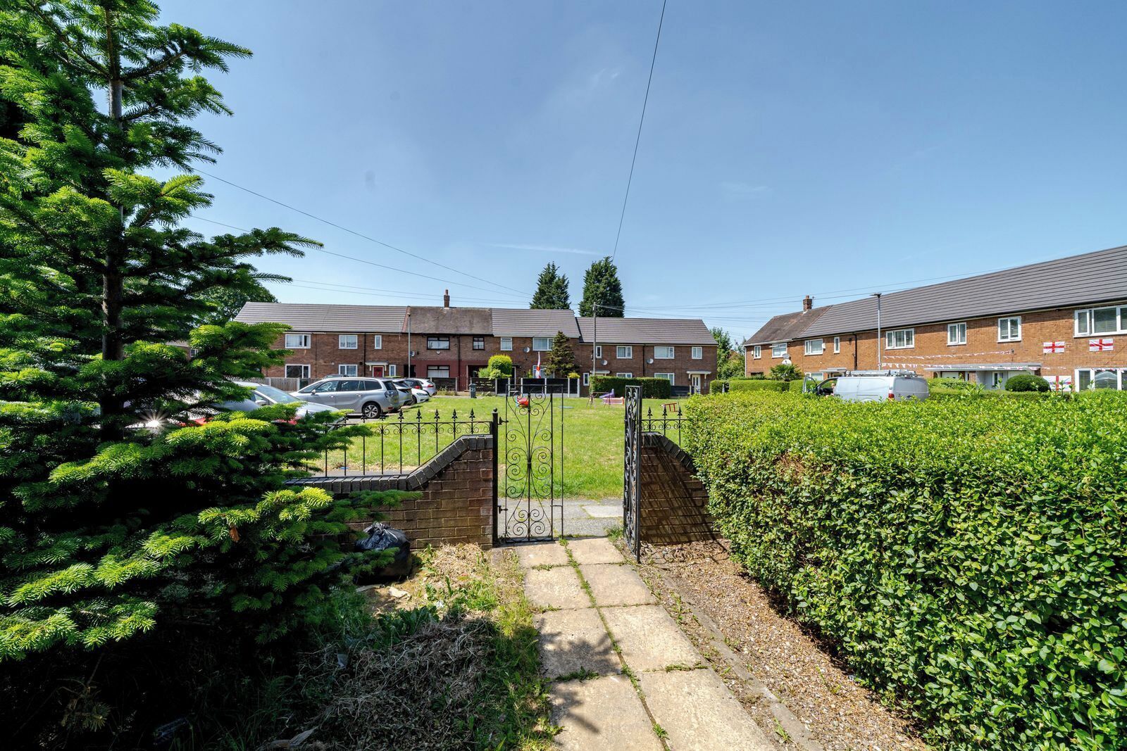 A residential area with houses, a gated entrance, and parked cars.