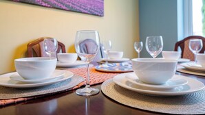 Una mesa de comedor dispuesta con cuencos, platos y copas de vino blancos, y un mantel tejido debajo.