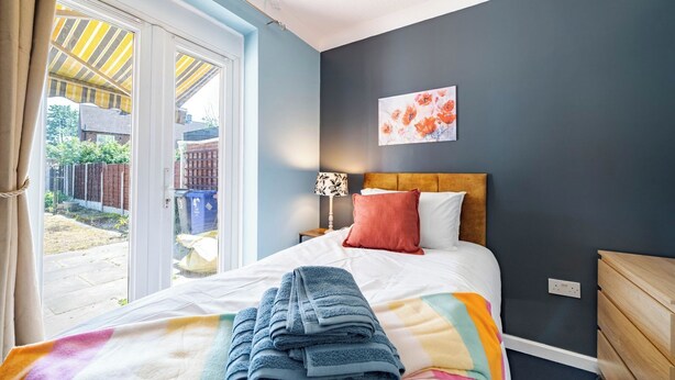 Un dormitorio con cama, mesita de noche, lámpara, una obra de arte en la pared y vistas al exterior.