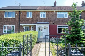 A two-story residential building with a red brick facade, white-framed windows, and a front door with a small porch. - Wythenshawe Stay | Airport & Hospital | Parking (Greater Manchester)