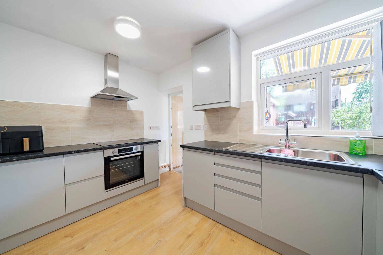 A modern kitchen with a built-in oven, a stainless steel range hood, and a window with striped curtains.