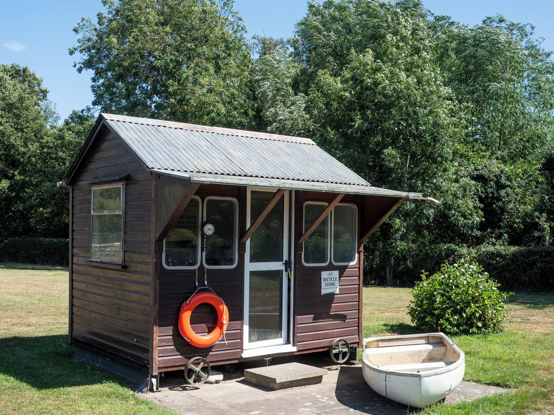 A small wooden structure with a metal roof, a bicycle storage sign, and a tire hanging on the side.