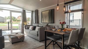 A modern living room with a sofa, a dining table with chairs, a coffee table, and a large window with curtains.