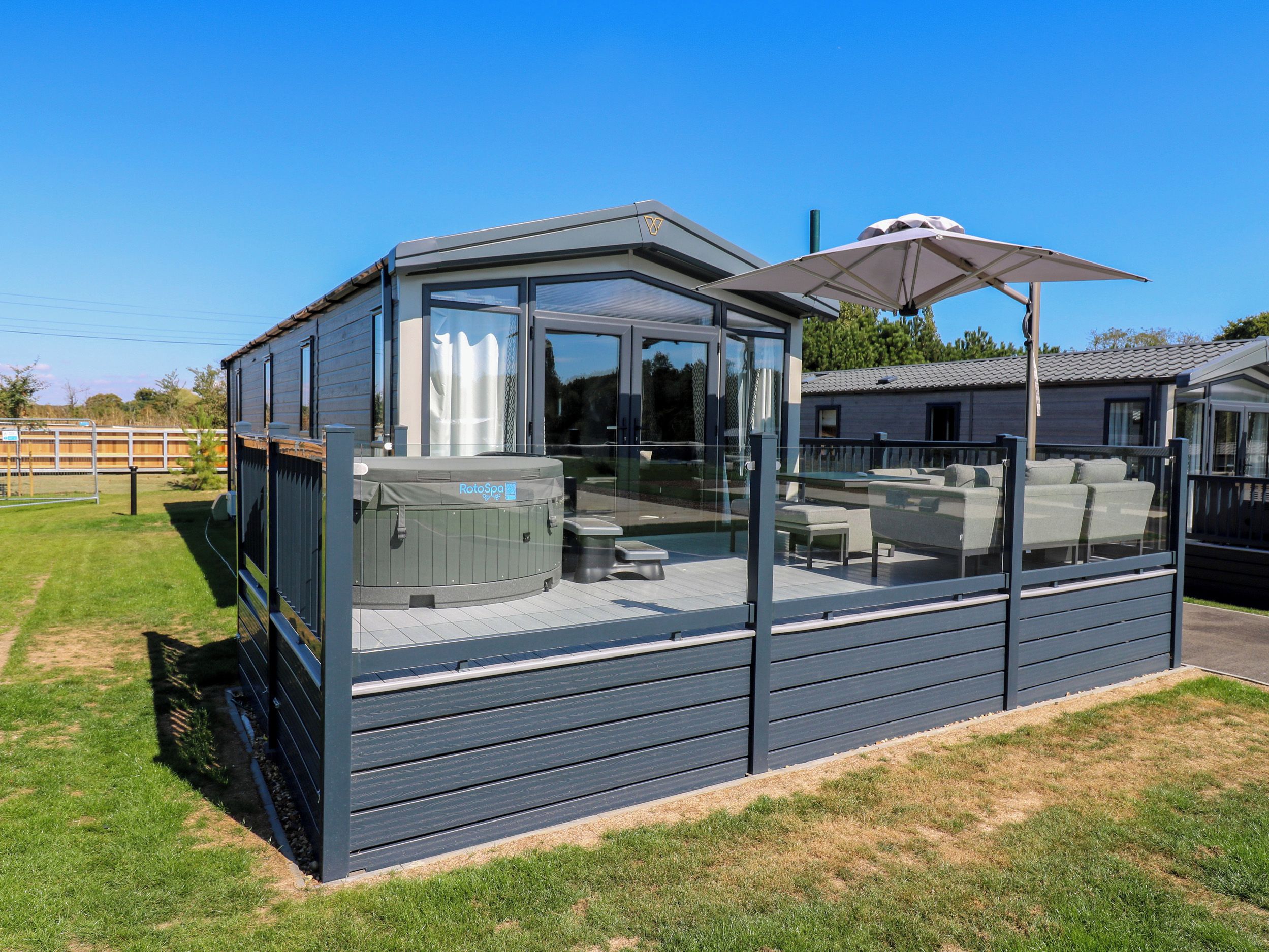 Ein moderner Außenbereich mit Whirlpool, Glasumrandung, Sitzgelegenheiten und Sonnenschirm.