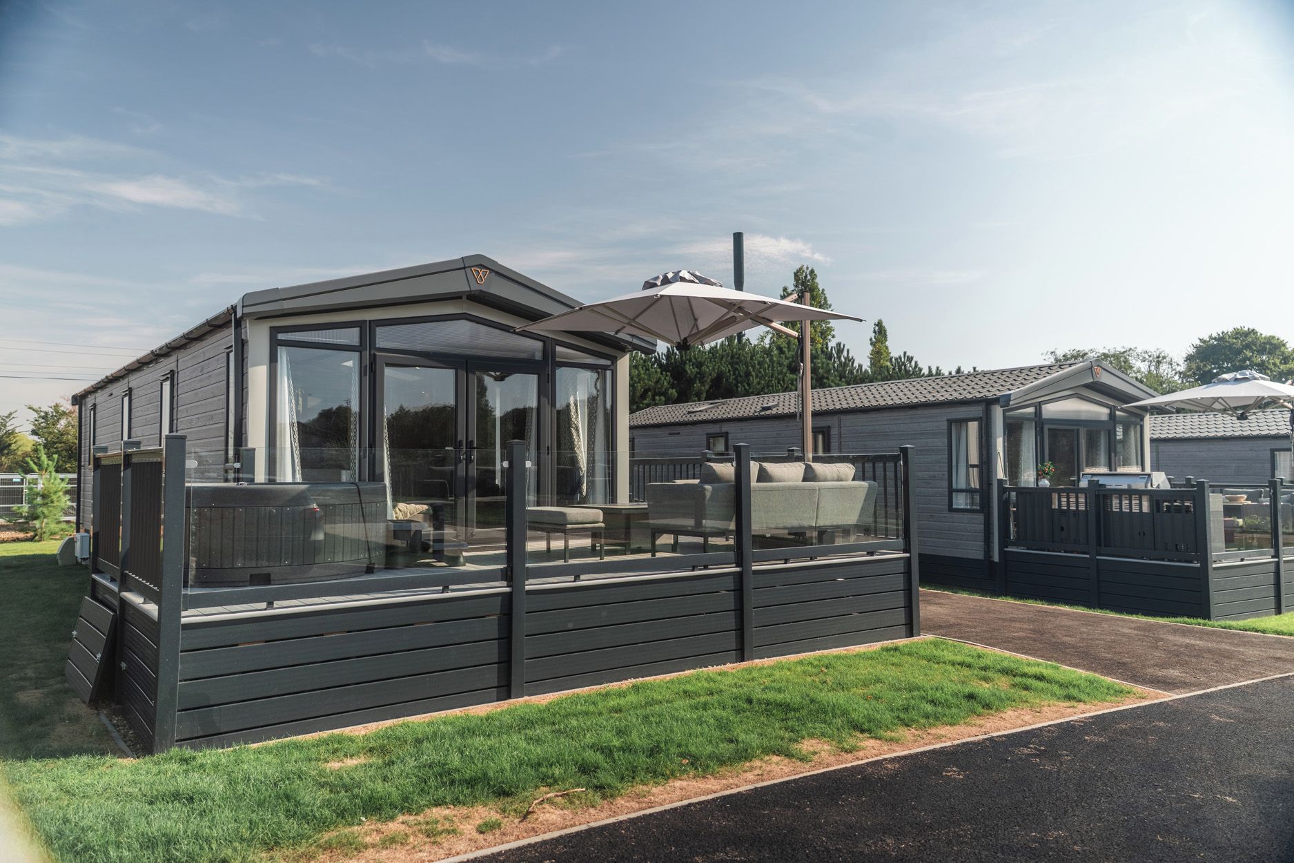 Una casa móvil moderna de un piso con un porche acristalado, una parrilla empotrada y una zona de estar cubierta al aire libre.