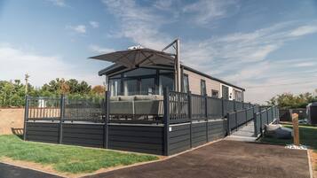 Una casa móvil moderna con un porche cubierto, una pequeña terraza y un ventanal visible.