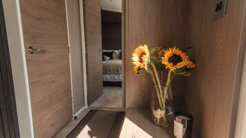 Ein Flur mit einer Holztür, einem Bett im Hintergrund und einer Vase mit Sonnenblumen auf einem Regal.