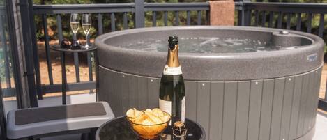 Un jacuzzi con una botella de champán y un cuenco de patatas sobre una mesa.