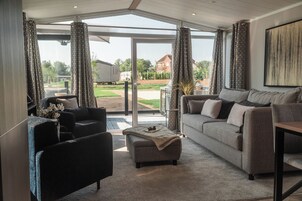 Una sala de estar moderna con un sofá gris, un sillón negro y una mesita de centro. Hay un ventanal con cortinas estampadas y vistas a una zona residencial.