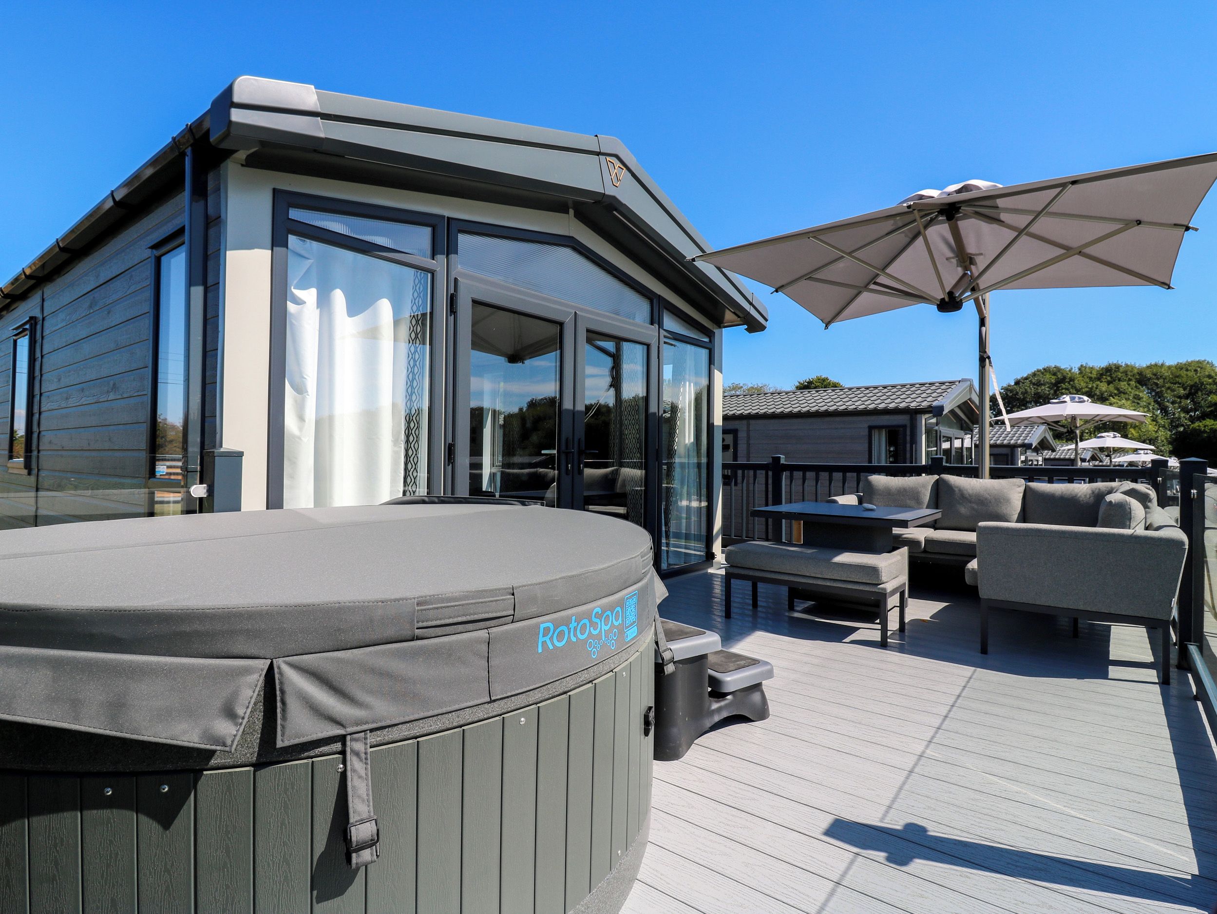 Eine Terrasse mit Sitzgelegenheiten im Freien, einem Whirlpool und einem überdachten Bereich mit Sonnenschirmen.
