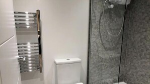 Ein modernes Badezimmer mit Toilette, einem chromfarbenen Handtuchhalter und einer Duschkabine.