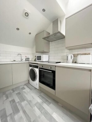A modern kitchen with a washing machine, oven, microwave, and cabinets. - Manchester Base | Heaton Park & Shops | Parking (Harpurhey)