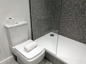 A modern bathroom with a toilet, a roll of toilet paper, and a bathtub. - Manchester Base | Heaton Park & Shops | Parking (Harpurhey)