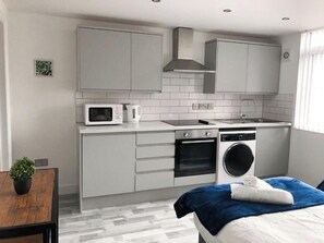 A compact kitchen with a microwave, kettle, oven, and washing machine. - Harpurhey Stay | Park & City Access | Heaton Park (Harpurhey)
