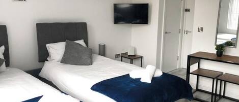 A hotel room with two beds, a TV, a desk, and a mirror.