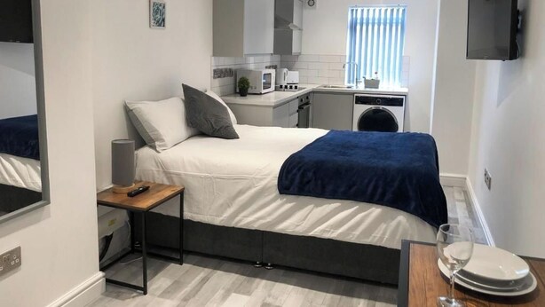 Una camera d'albergo compatta con un letto, un comodino e un angolo cottura.