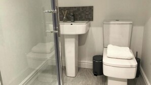 Un bagno con cabina doccia in vetro, lavandino bianco e water.