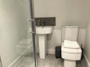 Ein Badezimmer mit Duschkabine aus Glas, einem weißen Waschbecken und einer Toilette.