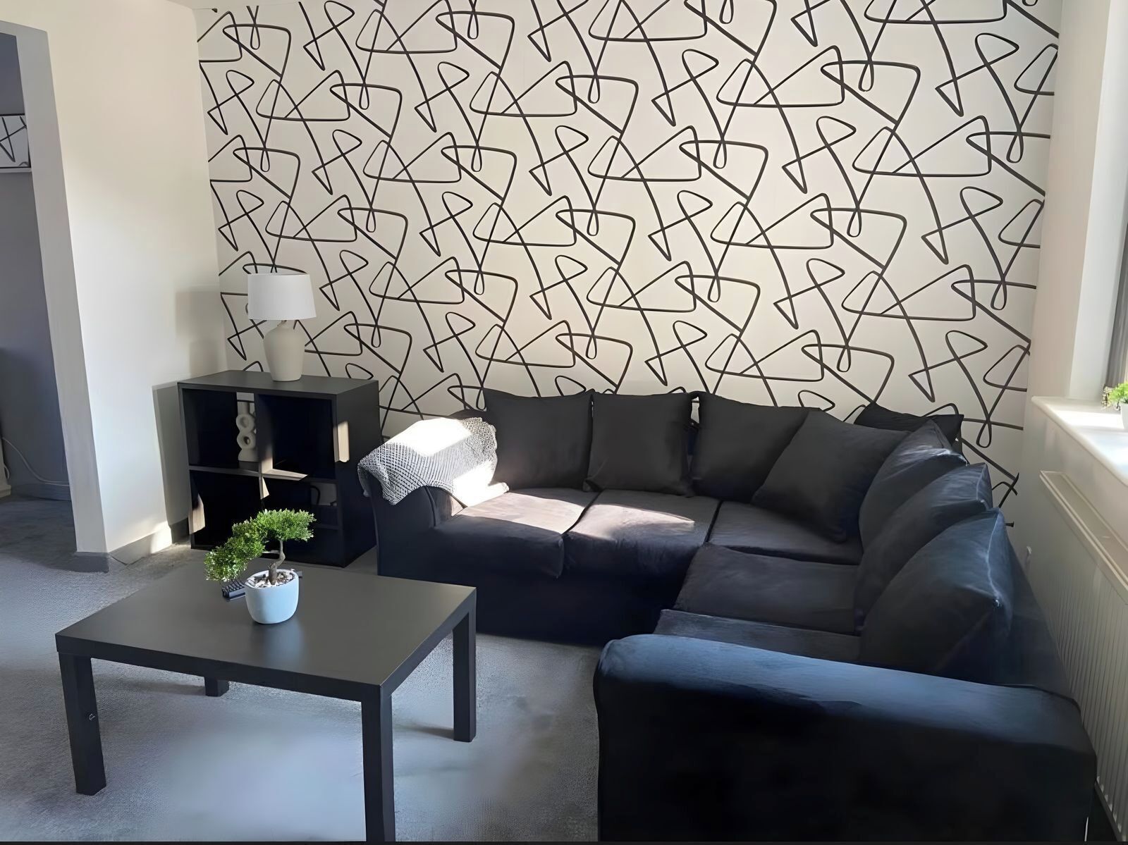 A modern living room with a sectional sofa, a small coffee table, a side table, and a decorative wall with geometric patterns.