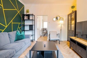 Un salon moderne avec un canapé gris, une table basse noire, une bibliothèque, un meuble pour la télévision et un lampadaire.