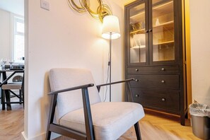 Un salon moderne avec un fauteuil de couleur claire, un meuble en bois foncé doté de portes en verre et un lampadaire.