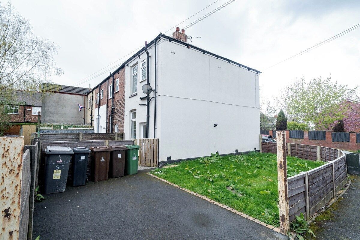 A residential area with a white building, a fenced yard, and multiple trash bins.