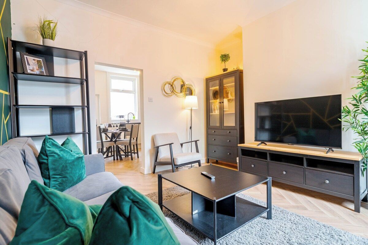 A modern living room with a sofa, coffee table, TV, and a dining area in the background.