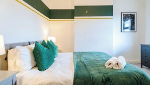 Un lit bien fait, avec des oreillers et une couverture, une table de chevet avec une lampe, et un tableau encadré au mur.