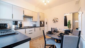 Une cuisine moderne avec des meubles blancs, un plan de travail noir et un coin repas avec une table mise pour deux personnes.